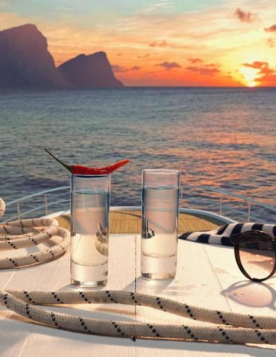 Two vodka shot glasses, one with a pepper laying on top of it. Served on top of a table with a rope and sunglasses, on the top level of a mega yacht.
