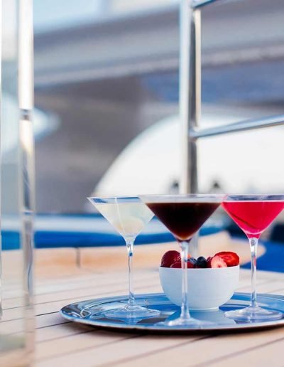 Three different fruity martini drinks on a silver tray with a bowl of cut berries.